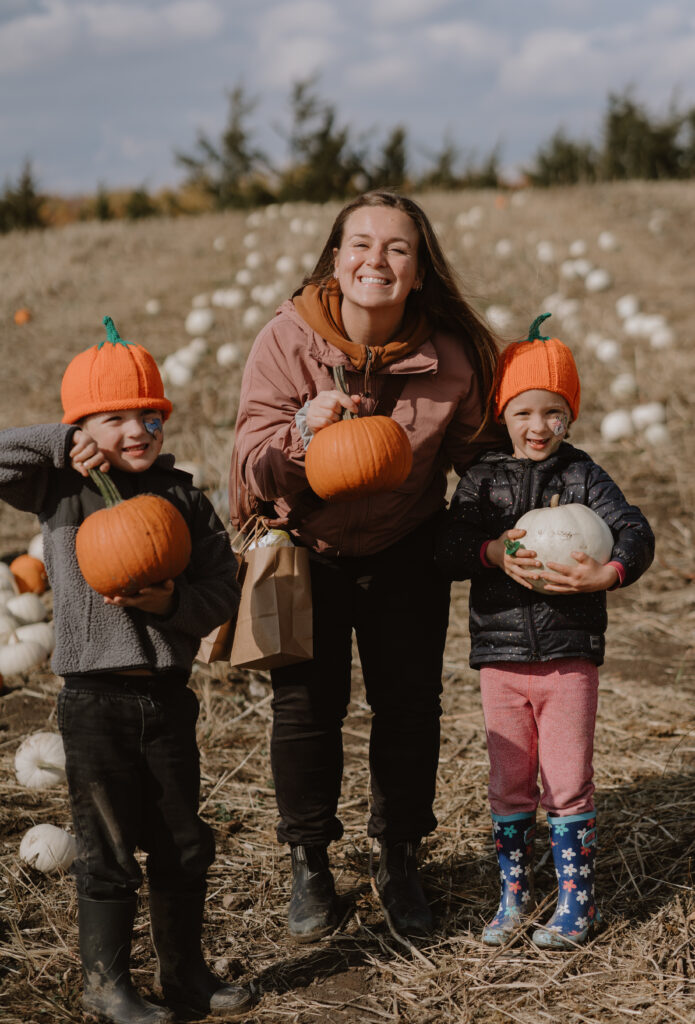 mom and two kids smile for the camera holding pumpkins