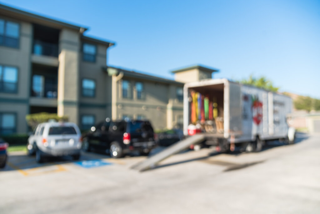 Blurred image of parked truck with open door, loading ramp waiting to transport for apartment moving. Relocate home, condominiums, housing, re-arranging furniture service/work concept background.