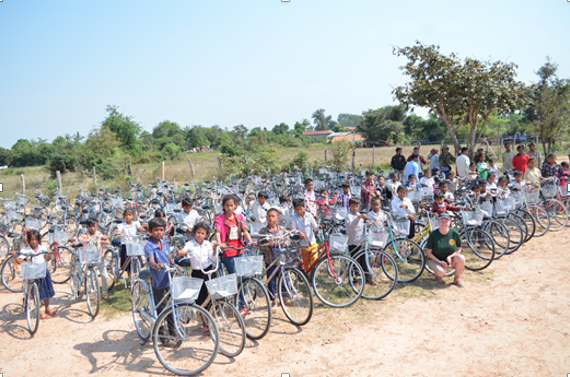 Children in school uniforms with bicycles at an outdoor event in a rural area.