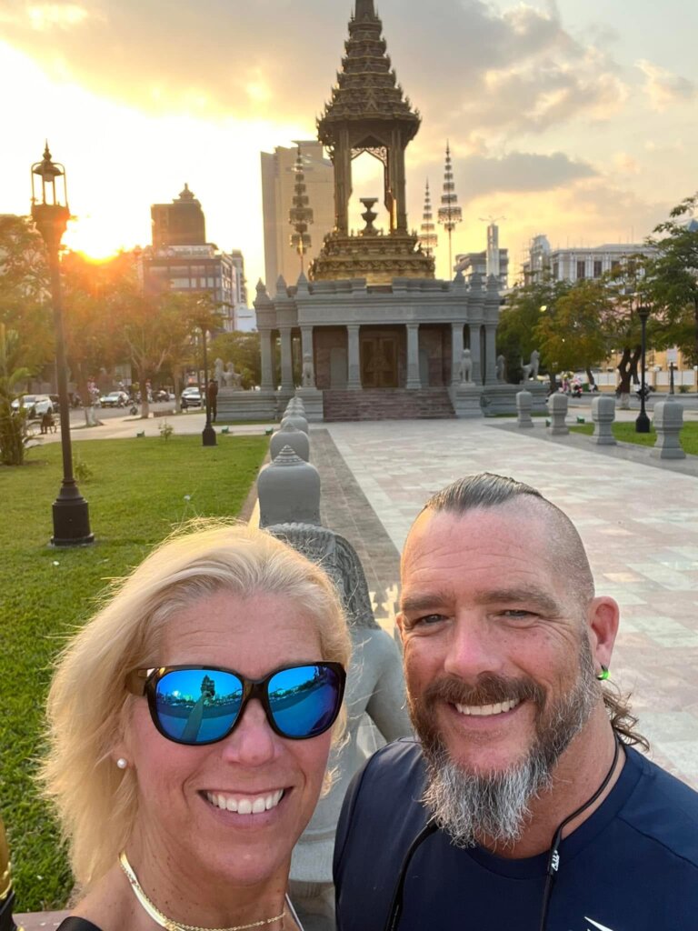 Jen and Pat Menard smiling in front of a monument at sunset.