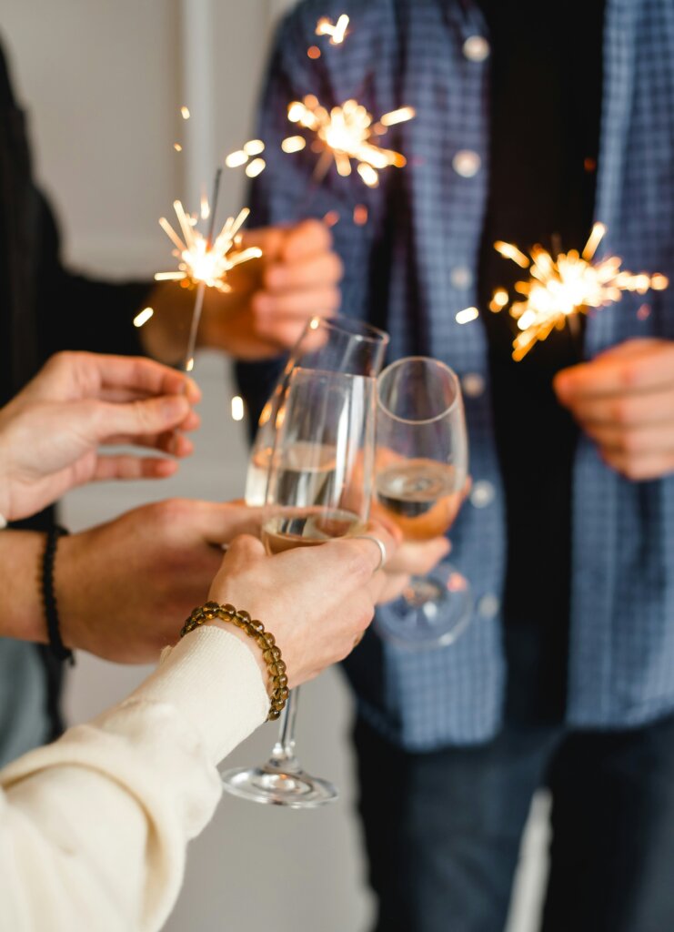 3 people with sparklers and champagne clinking their glasses together to celebrate the new year