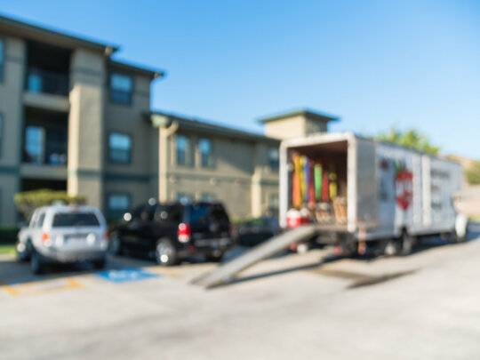 Blurred image of parked truck with open door, loading ramp waiting to transport for apartment moving. Relocate home, condominiums, housing, re-arranging furniture service/work concept background.